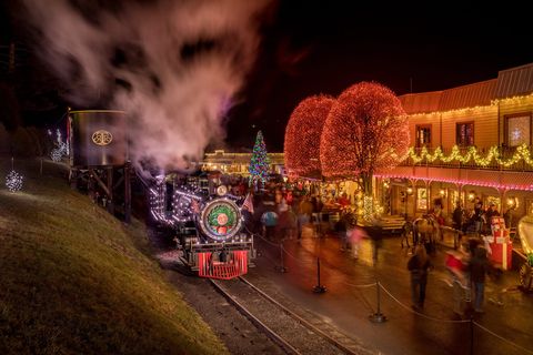 old fashion train covered in christmas lights pulling into a christmas town