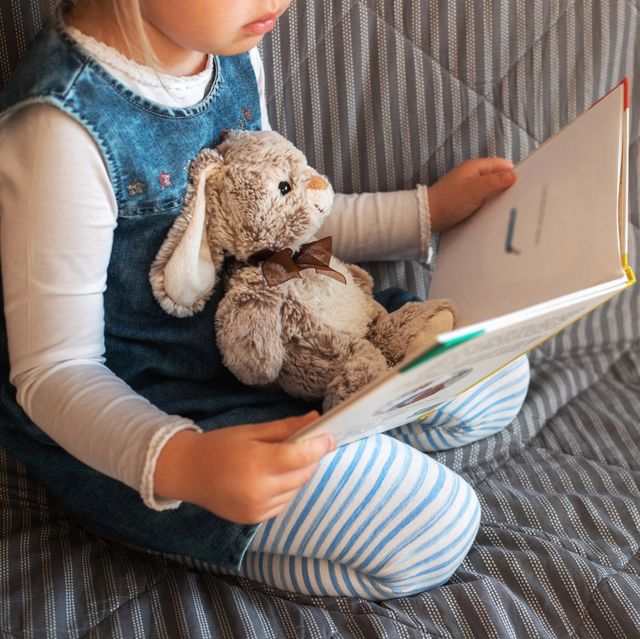 little girl reading favorite book at home with her toy rabbit