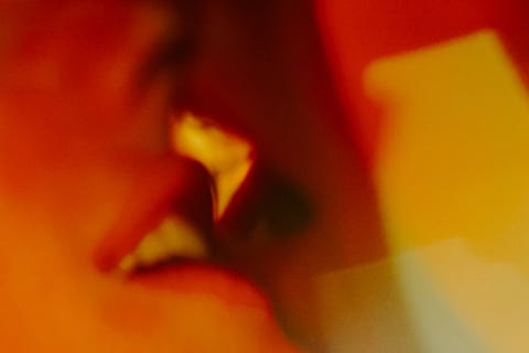 young beautiful woman is kissing her boyfriend gently their eyes are closed couple is illuminated with bright multicolored lights
