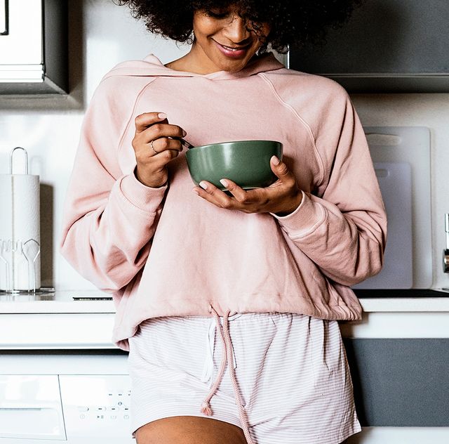 woman wearing pajamas eating cereal in kitchen