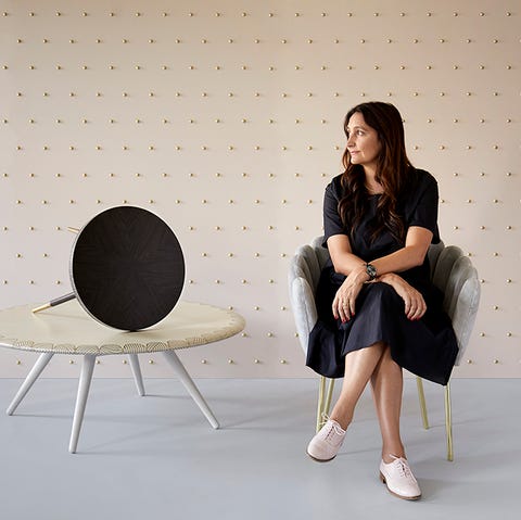 Portrait of Bethan Gray, seated in chair in front of studded wall and next to stacked tables