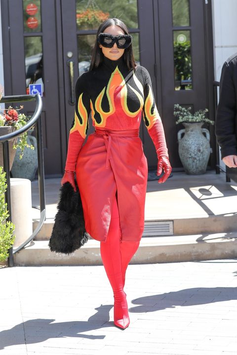 kim kardashian wearing a long sleeve black shirt with flames on it, leather red gloves, a red leather skirt and red boots that cover her entire leg