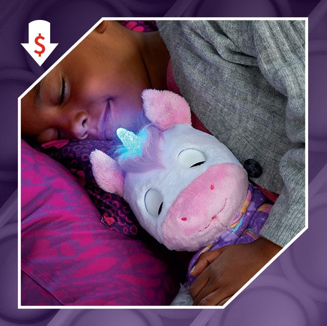 young girl holding unicorn toy in bed and kid's hand playing with fire engine toy