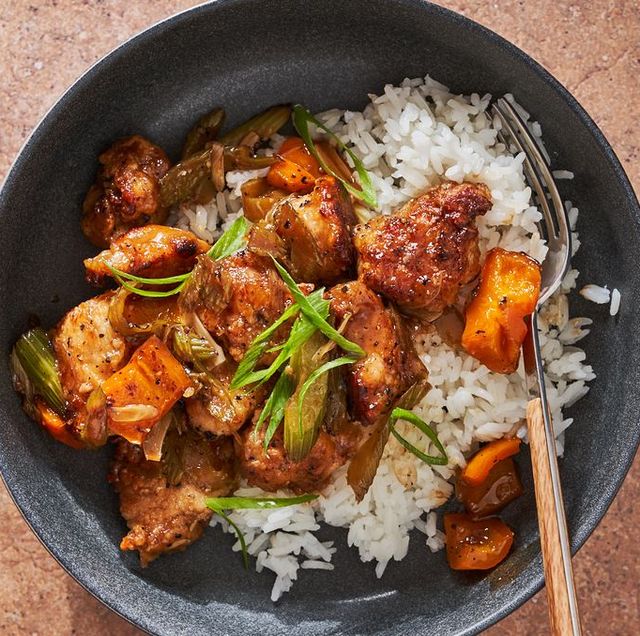 black pepper chicken with orange peppers, celery and scallions over white rice in a black bowl