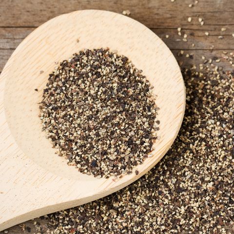 coarse ground black pepper on a wooden spoon and spilled on an old, weathered wood surface