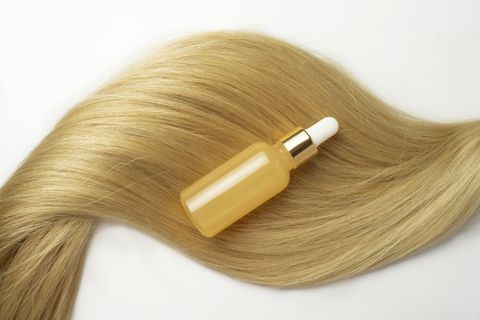 a blonde tress with a natural oil or serum for hair care lying on it