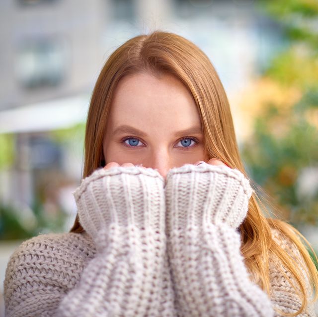 blonde woman with blue eyes in warm chunky knit sweater covers her mouth with hands