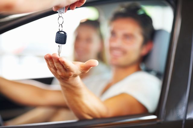 blurred couple with man receiving car key from salesman