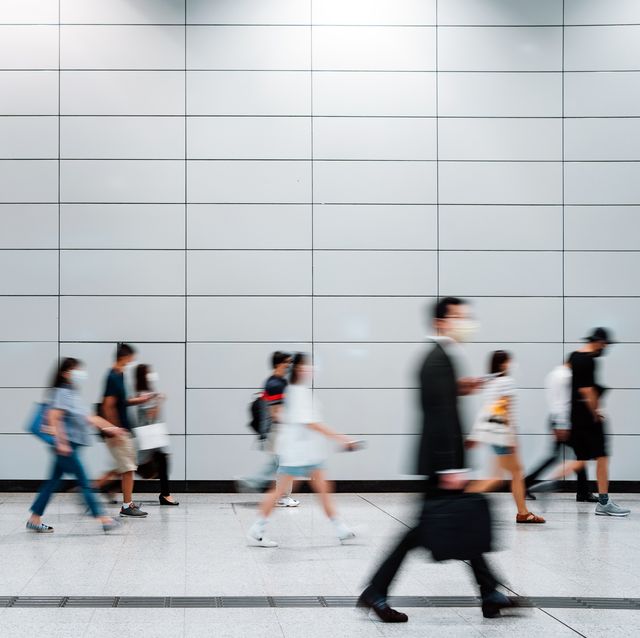 blurred motion of a crowd of busy commuters with protective face mask walking through platforms at subway station during office peak hours in the city