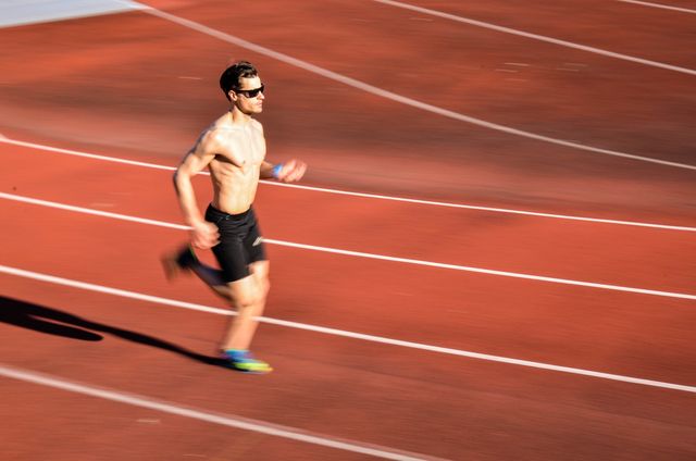 blurred motion of shirtless man running on track
