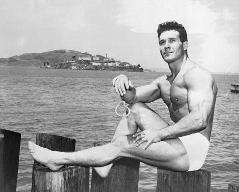 Jack LaLanne Sitting on Post Near Water