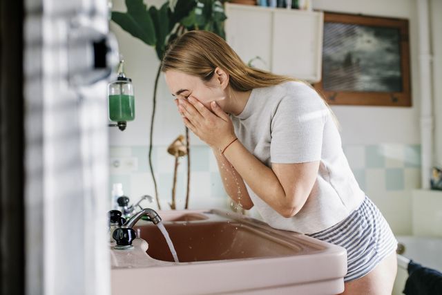 woman bending over bathroom sink washing her face