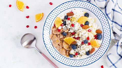 bowl of flakes with cottage cheese and yogurt, blueberryes and pomegranate on white table fitness food overhead, top view, flat lay