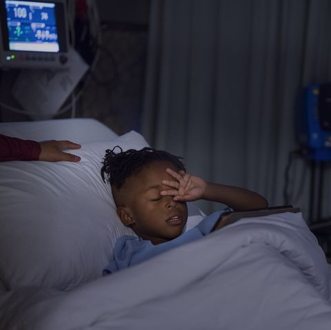 Boy rubbing eyes while lying on bed at ward
