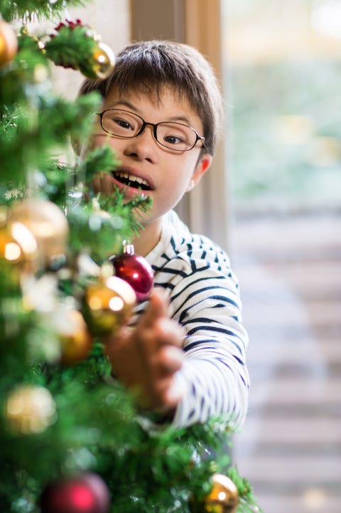 a boy with downs syndrome hanging decorations on a christmas tree