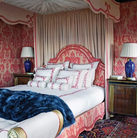 lush bed with curtains and scalloped headboard baseboard upholsterd in red floral that matches wallpaper behind bed is made with white sheets and stacks of pillows with red embroidered trim a