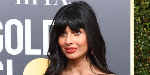 A photo of Jameela Jamil at an awards ceremony in a strapless pink dress, smiling on the red carpet.