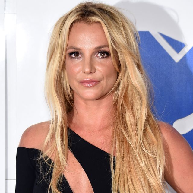 britney spears, a young woman standing looking at the camera with left hand on hip, long blonde hair worn down in loose waves, wearing an asymmetrical long black dress with thigh split