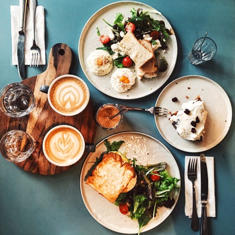 brunch for two people with avocado toast, fried egg, salad, cappuccino and carrot cake served on the table, high angle view