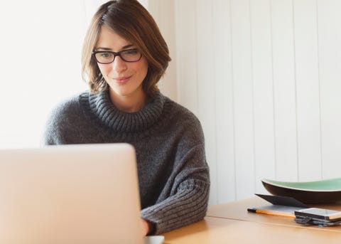 Brunette woman in sweater using laptop at table