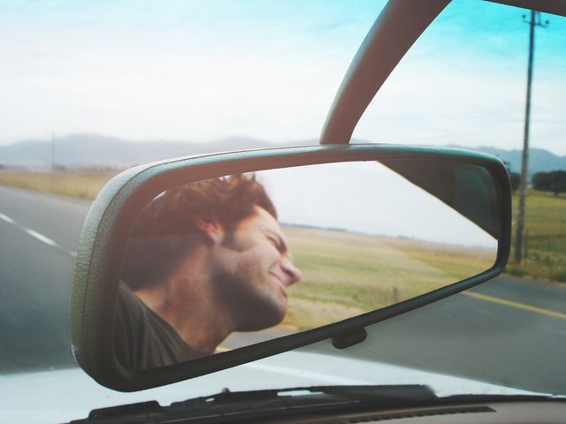 hombre reflejado en el espejo interior del coche conduciendo con viento