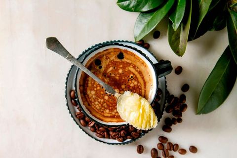 bulletproof coffee keto diet coffee in blue ceramic cup with organic ghee butter in spoon with beans and green branch over white marble background flat lay space