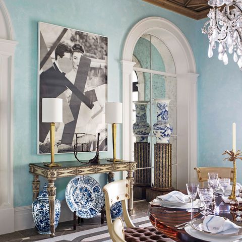 classic nterior with geometric rug under a dining table set with suhioned chairs and a sideboard with two modern lamps and large blue and white china displayed below