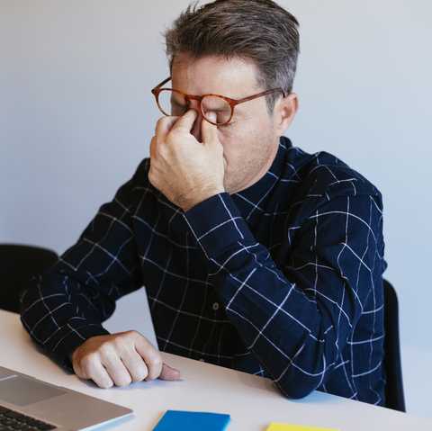 Businessman at desk in office rubbing his eyes