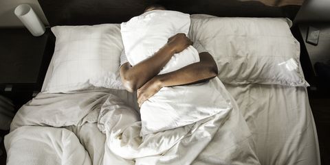 Man knuffelt met kussen in zijn bed onder deken.