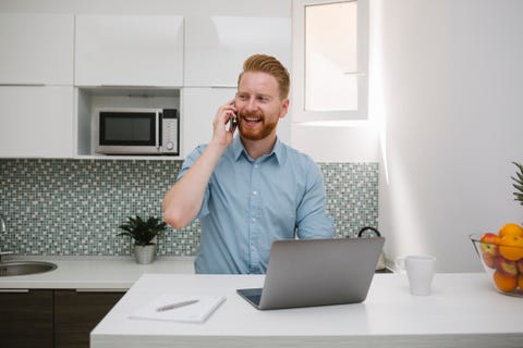 Businessman with laptop talking on the phone in his kitchen