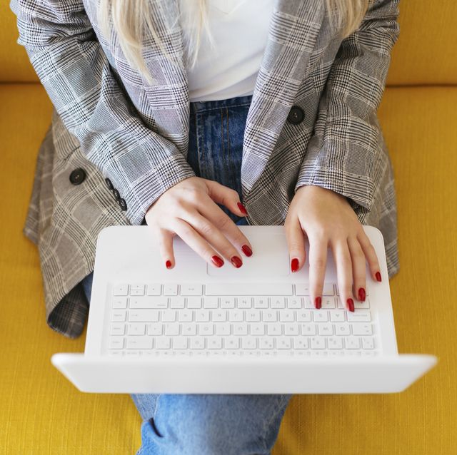 businesswoman sitting on yellow couch, using laptop