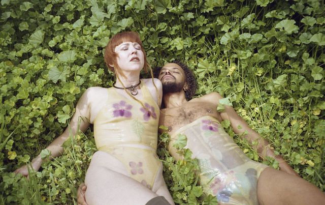 a man and woman lie in the grass in bdsm attire