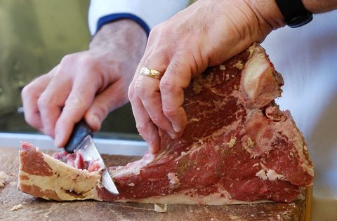 A butcher trims fat off a prime rib beef