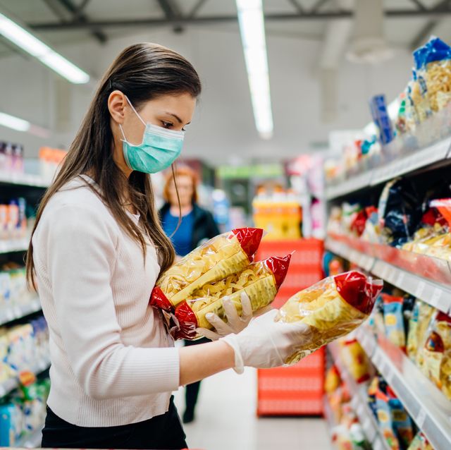 Buyer wearing a protective mask.Shopping during the pandemic quarantine.Nonperishable smart purchased household pantry groceries preparation.Woman buying few pasta packages.Budget pastas and noodles.