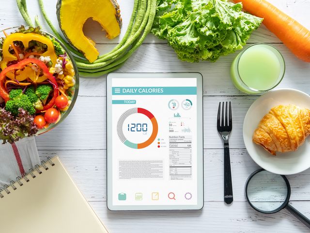 calories counting , diet , food control and weight loss concept tablet with calorie counter application on screen at dining table with salad, fruit juice, bread and vegetable