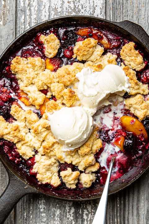 berry peach cobbler in a black cast iron skillet topped with vanilla ice cream