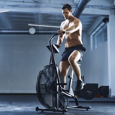 Athletic man doing HIIT workout on airbike at gym