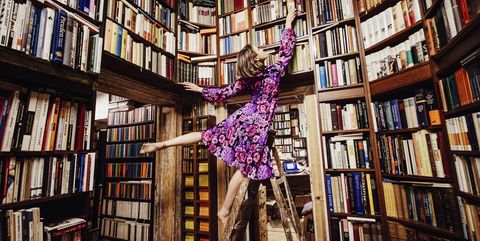 Carefree woman on ladder reaching for book in library