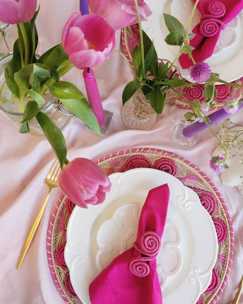 a table setting with pink napkins, pastel pink tablecloth and flowers