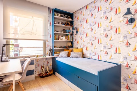 children's bedroom with blue trundle bed and wallpaper with figures of sailboats