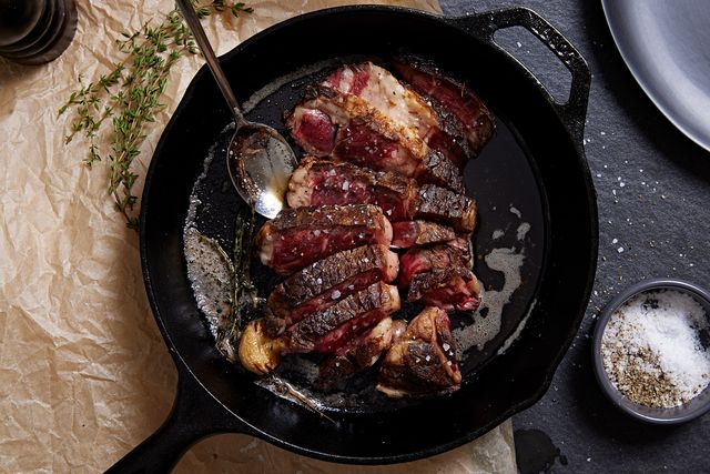 sliced boneless steak garnished with garlic and thyme in a black cast iron pan