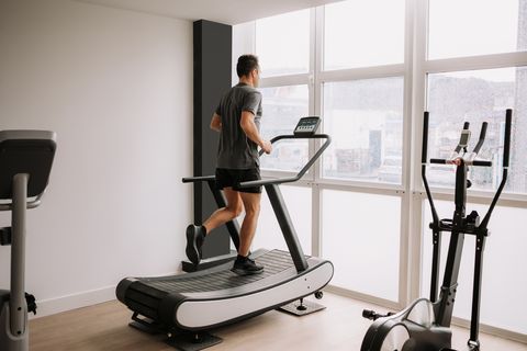 Caucasian adult man runs on treadmill in gym next to a large window