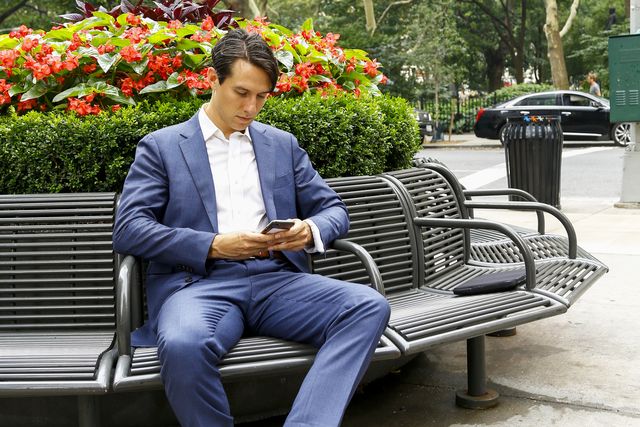 caucasian businessman on park bench texting on cell phone