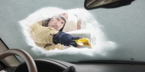 caucasian man scraping snow off car windshield