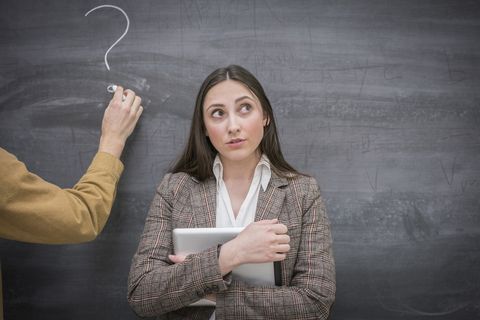 caucasian woman thinking next to question mark on blackboard in classroom