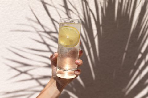 glass of water with lemon in women's hand against background with shadows of palm tree