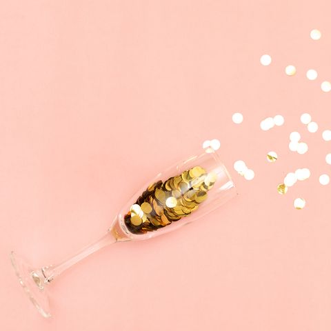 champagne glass with golden confetti tinsel on pink background
