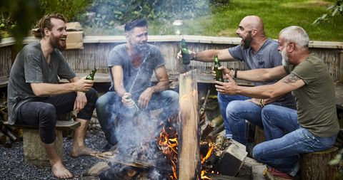 Cheerful friends sitting together at camp fire drinking beer