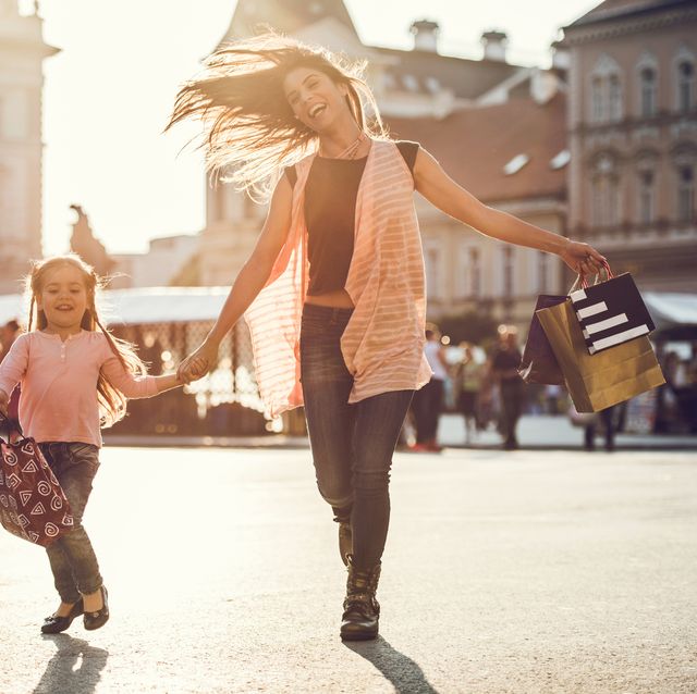 Cheerful woman and little girl running with shopping bags.