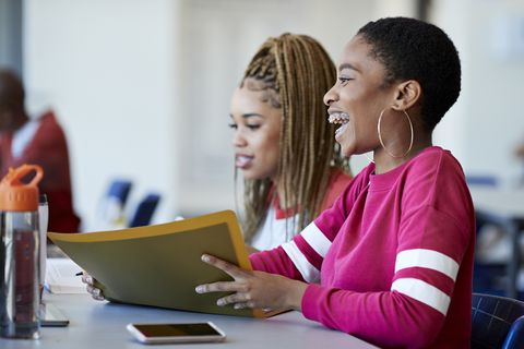 cheerful woman sitting by friend in classroom